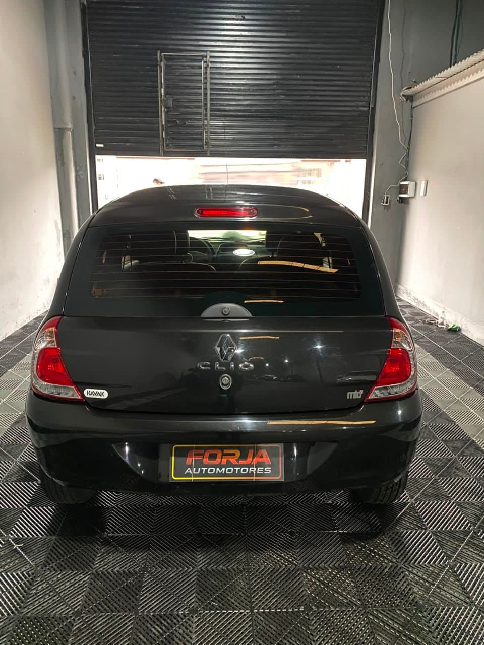 Renault Clio negro de atrás, con la persiana del local de fondo