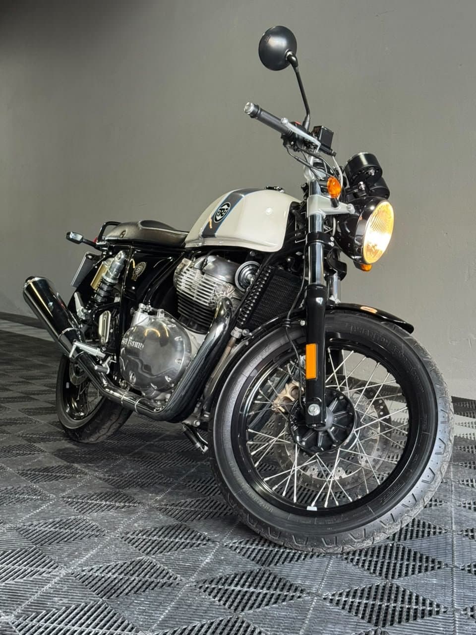 Royal Enfield Continental GT 650 blanca, frente tres cuartos con el faro encendido, en el showroom